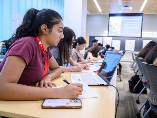 Student working on laptop and writing
